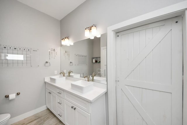 full bathroom featuring double vanity, a sink, toilet, and baseboards