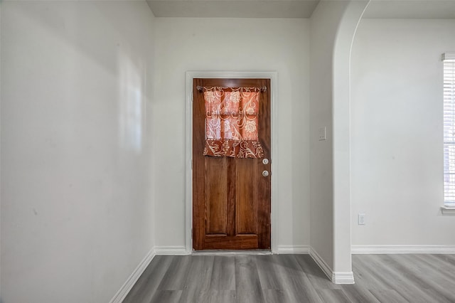 entryway with arched walkways, baseboards, and wood finished floors