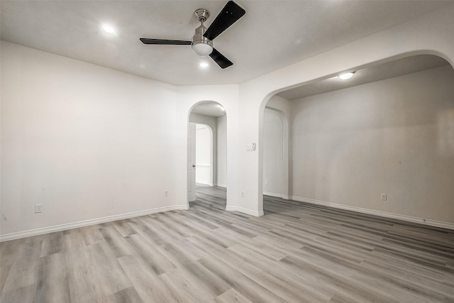 empty room featuring baseboards, arched walkways, light wood-style flooring, and a ceiling fan