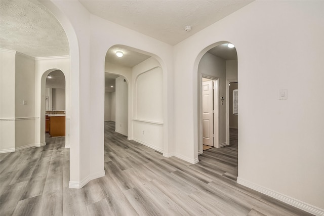 spare room with baseboards, light wood-style flooring, and a textured ceiling