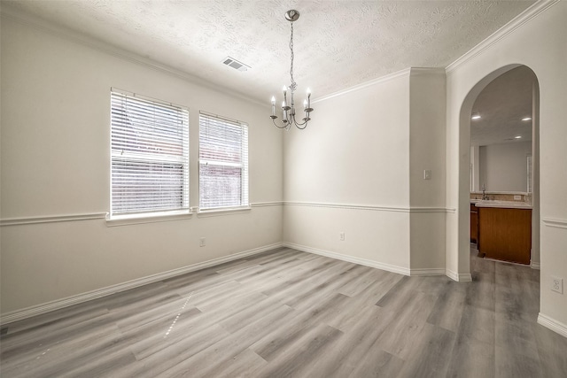 spare room with light wood-style floors, visible vents, arched walkways, and ornamental molding