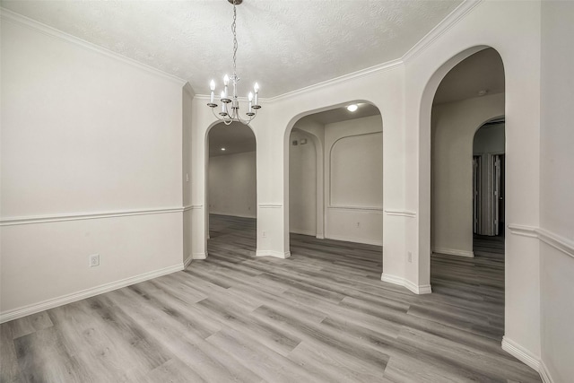 unfurnished dining area with a notable chandelier, a textured ceiling, ornamental molding, and wood finished floors