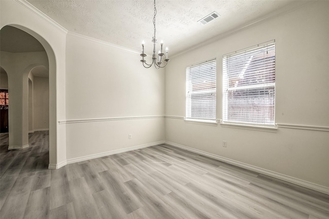 empty room featuring a textured ceiling, visible vents, arched walkways, and wood finished floors