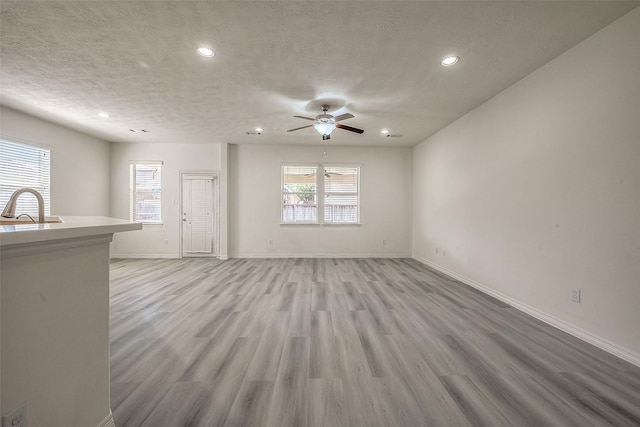 unfurnished living room featuring a textured ceiling, recessed lighting, a sink, baseboards, and light wood finished floors