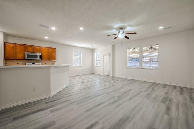 unfurnished living room with a ceiling fan, visible vents, light wood-style flooring, and baseboards