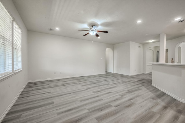 unfurnished living room featuring arched walkways, baseboards, a ceiling fan, and light wood-style floors