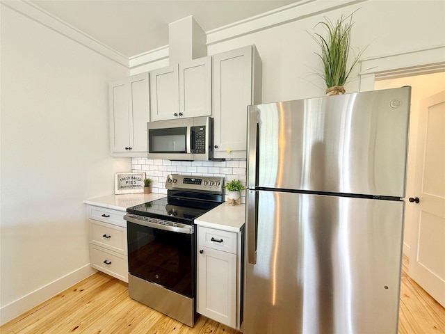 kitchen with light countertops, appliances with stainless steel finishes, ornamental molding, decorative backsplash, and light wood finished floors