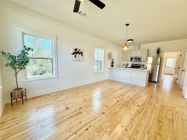 kitchen with light wood finished floors, backsplash, appliances with stainless steel finishes, ornamental molding, and a peninsula