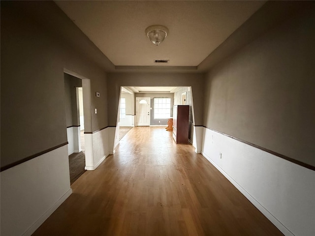 hall featuring wood finished floors, visible vents, and baseboards