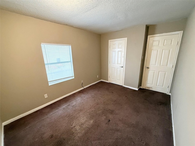 unfurnished bedroom with a textured ceiling, dark colored carpet, and baseboards