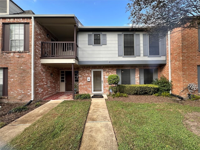 multi unit property with a front lawn, a balcony, and brick siding