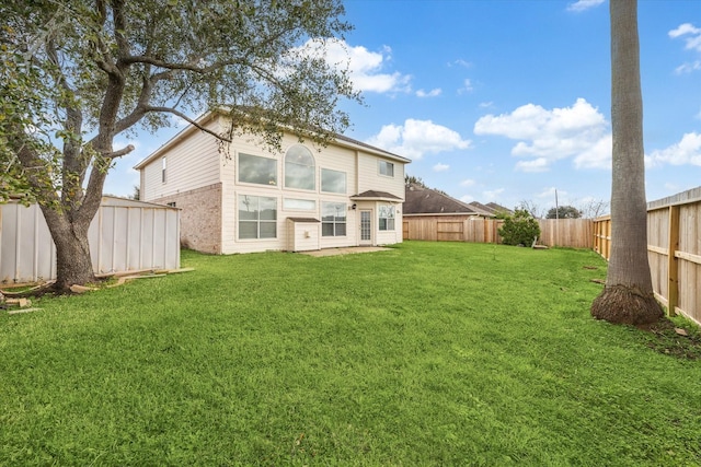 rear view of property with a fenced backyard, a lawn, and brick siding