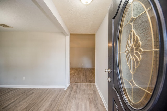 entryway featuring baseboards, a textured ceiling, visible vents, and wood finished floors