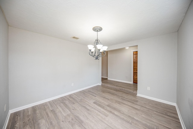 empty room with a notable chandelier, visible vents, a textured ceiling, light wood-type flooring, and baseboards