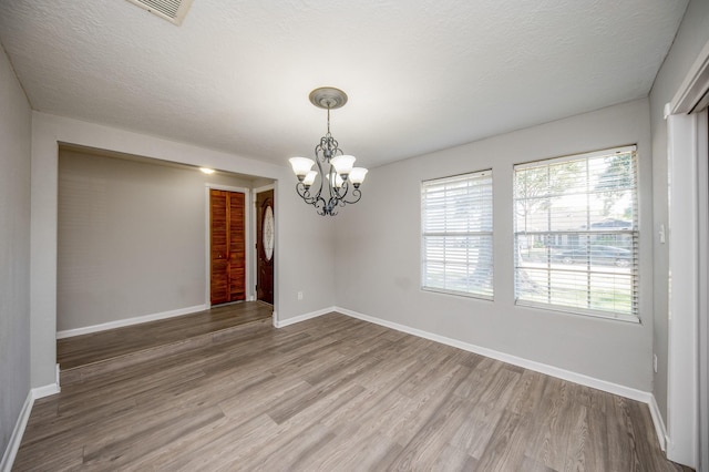 unfurnished room with baseboards, visible vents, wood finished floors, a textured ceiling, and a notable chandelier