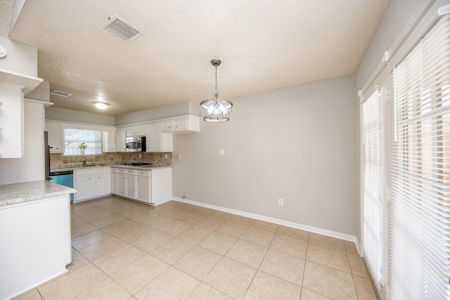 kitchen featuring tasteful backsplash, visible vents, stainless steel microwave, gas stovetop, and white cabinetry