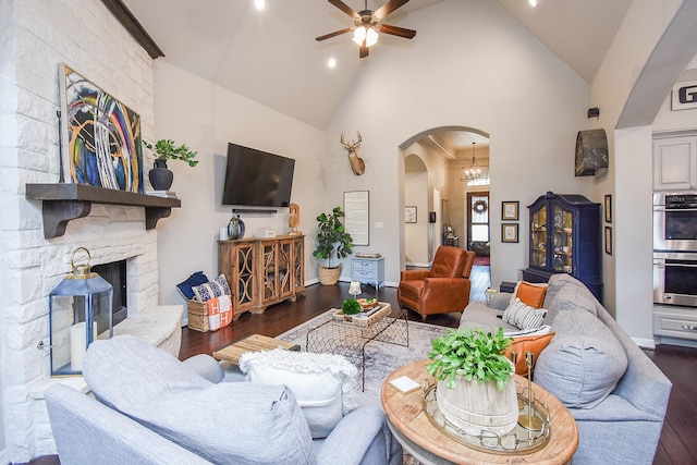 living area with a ceiling fan, arched walkways, a stone fireplace, and wood finished floors