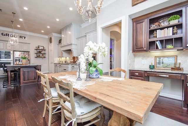 dining room featuring ornamental molding, arched walkways, dark wood finished floors, and a notable chandelier