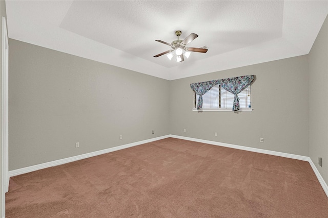 empty room with carpet, a raised ceiling, and baseboards