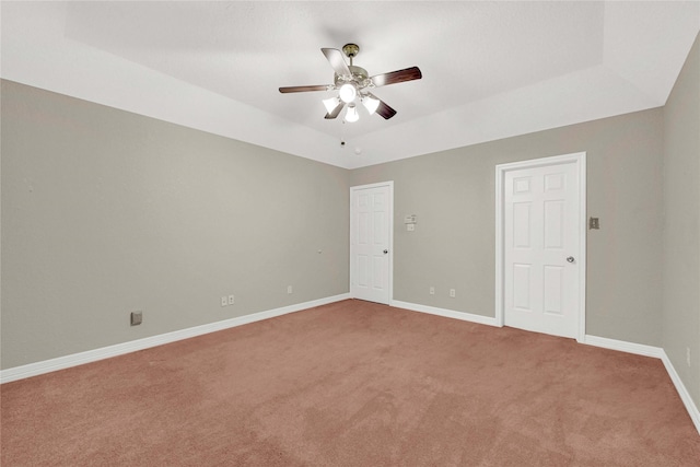 spare room featuring a ceiling fan, a tray ceiling, light colored carpet, and baseboards