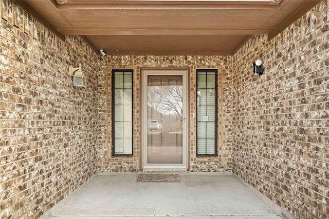 view of exterior entry featuring a patio and brick siding