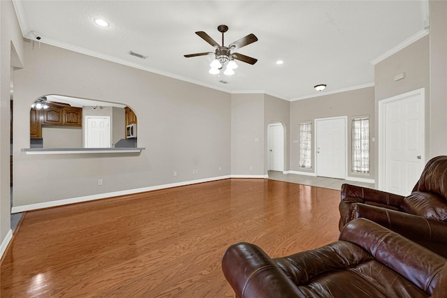 living room featuring arched walkways, wood finished floors, a ceiling fan, baseboards, and crown molding