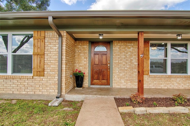 view of exterior entry with a porch and brick siding