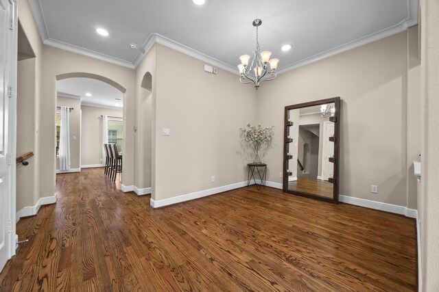 empty room with arched walkways, a chandelier, dark wood-type flooring, baseboards, and ornamental molding