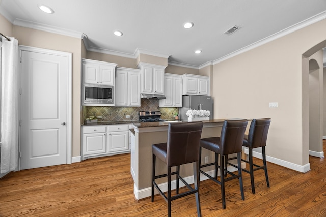 kitchen with white cabinets, appliances with stainless steel finishes, arched walkways, and a kitchen breakfast bar