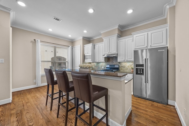 kitchen featuring under cabinet range hood, visible vents, appliances with stainless steel finishes, backsplash, and a center island