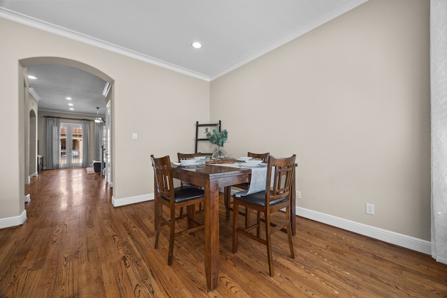 dining space featuring arched walkways, crown molding, baseboards, and wood finished floors