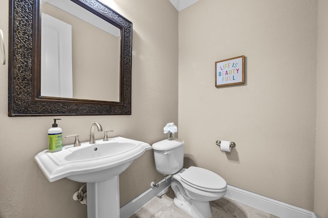 half bathroom featuring toilet, baseboards, a sink, and tile patterned floors