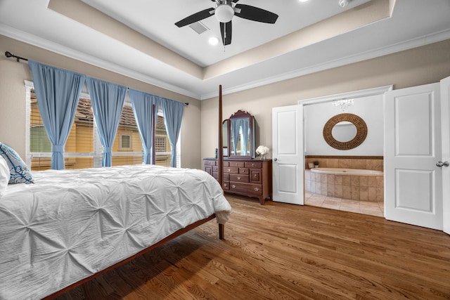 bedroom featuring ensuite bathroom, a tray ceiling, wood finished floors, and ornamental molding