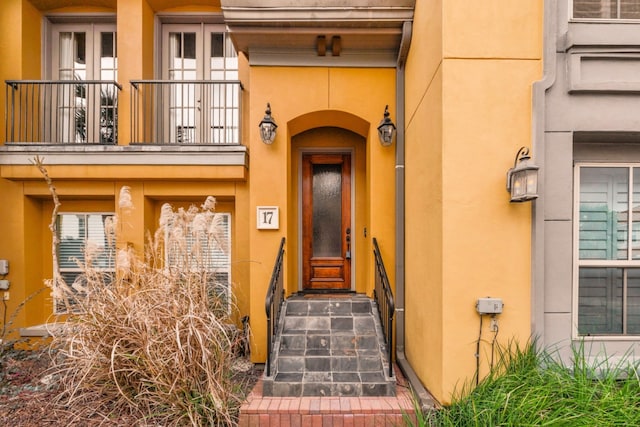 property entrance featuring a balcony, french doors, and stucco siding