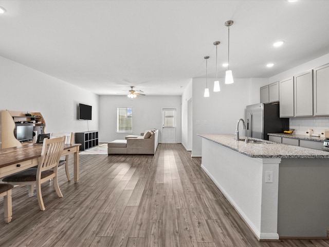 kitchen with light stone counters, stainless steel refrigerator with ice dispenser, gray cabinets, ceiling fan, and wood finished floors