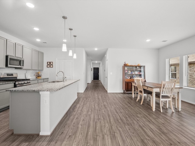 kitchen featuring gray cabinets, wood finished floors, appliances with stainless steel finishes, a sink, and light stone countertops