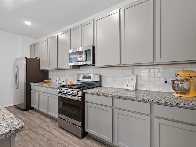 kitchen with light wood-type flooring, gray cabinets, stainless steel appliances, and decorative backsplash