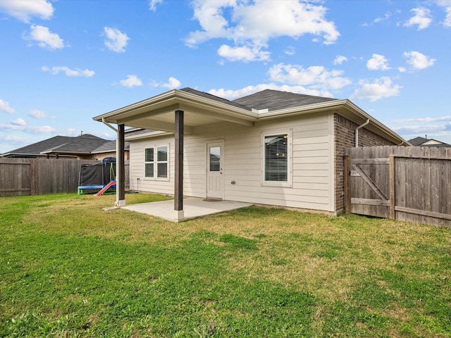 rear view of property featuring a trampoline, brick siding, a yard, a patio area, and a fenced backyard