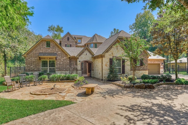 view of front of property featuring stone siding, an attached garage, a gate, fence, and brick siding