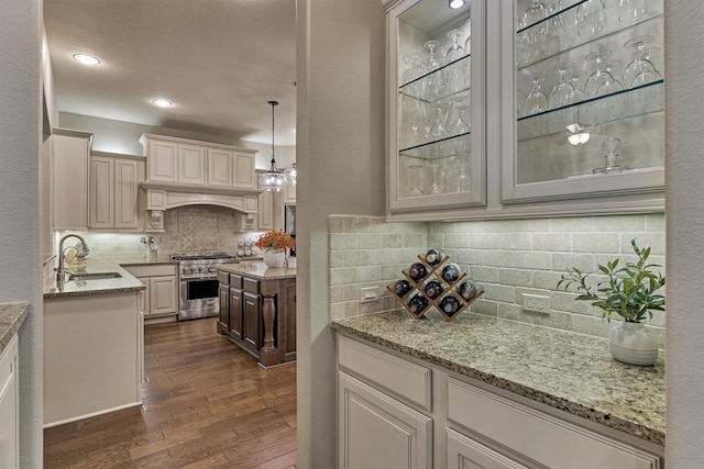 kitchen with glass insert cabinets, light stone counters, dark wood-style flooring, high end stainless steel range, and a sink