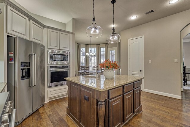 kitchen with visible vents, an island with sink, dark wood-type flooring, stainless steel appliances, and a sink