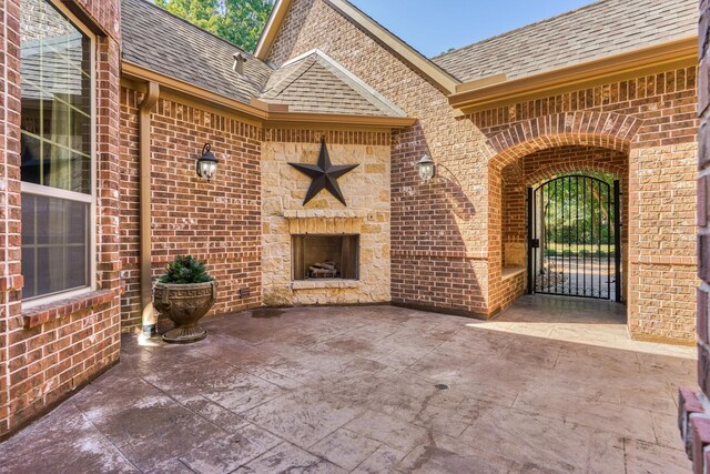 view of exterior entry with a shingled roof, a patio area, a gate, and brick siding