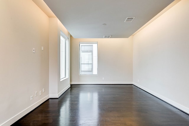 empty room with dark wood-style floors, visible vents, and baseboards