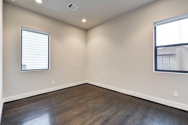 empty room with dark wood-type flooring, visible vents, plenty of natural light, and baseboards