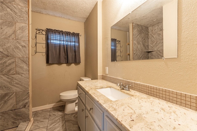 bathroom featuring toilet, a textured ceiling, vanity, tiled shower, and baseboards