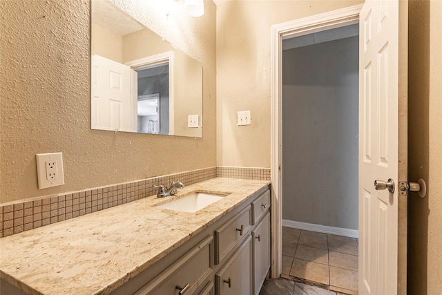 bathroom with a textured wall, baseboards, backsplash, and vanity