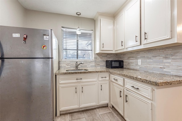 kitchen featuring tasteful backsplash, white cabinets, freestanding refrigerator, black microwave, and a sink