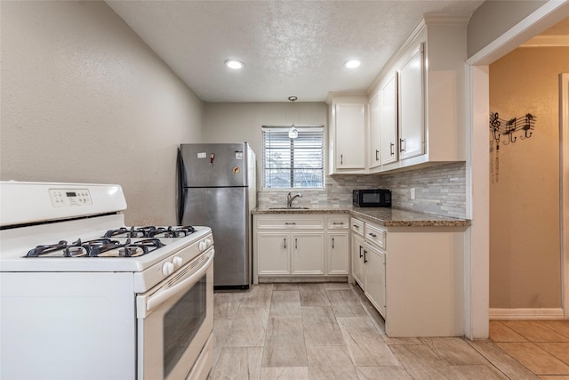 kitchen featuring white gas range, decorative backsplash, freestanding refrigerator, white cabinetry, and black microwave