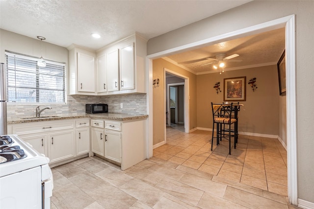 kitchen with black microwave, white range with gas stovetop, a sink, white cabinets, and decorative backsplash