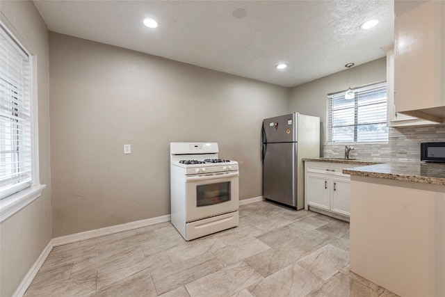 kitchen featuring white cabinets, decorative backsplash, freestanding refrigerator, light stone countertops, and gas range gas stove